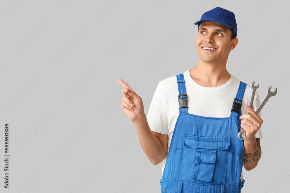 Male car mechanic with wrenches pointing at something on grey background