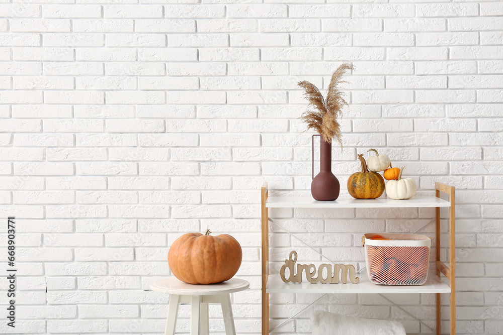 Vase with pampas grass and pumpkins on shelving unit near white brick wall