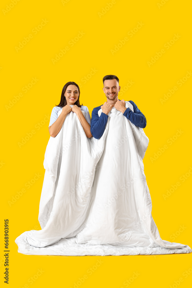 Young couple with soft blanket on yellow background