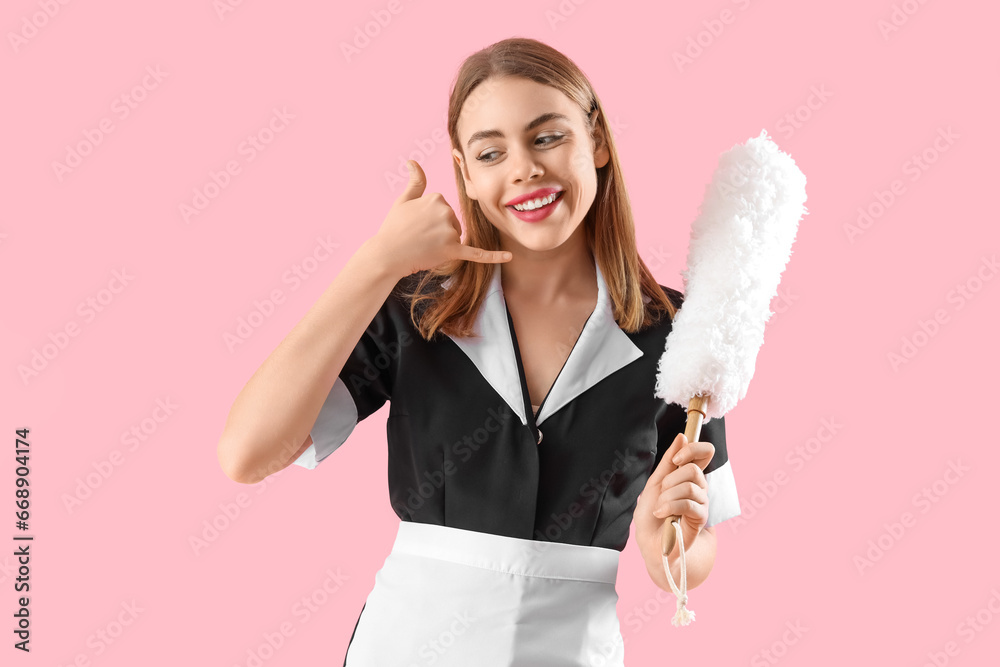 Beautiful female janitor with pp-duster showing  call me  gesture on pink background