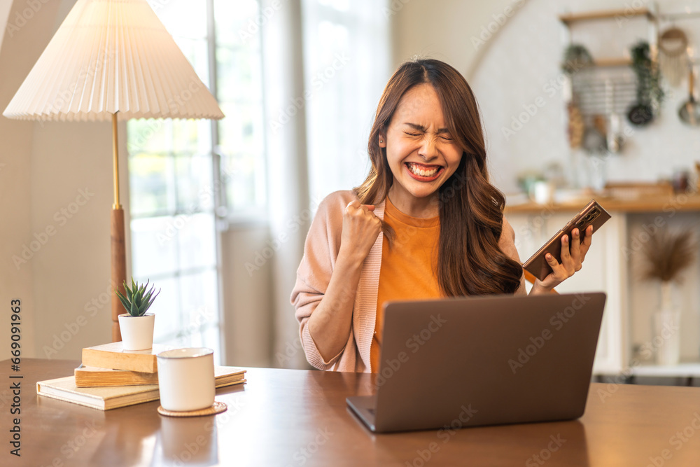 Young smiling asian woman happy relax use laptop conference work,learning education, shopping, study online, webinar, podcast,creative girl holding smartphone positive, success, excited at home