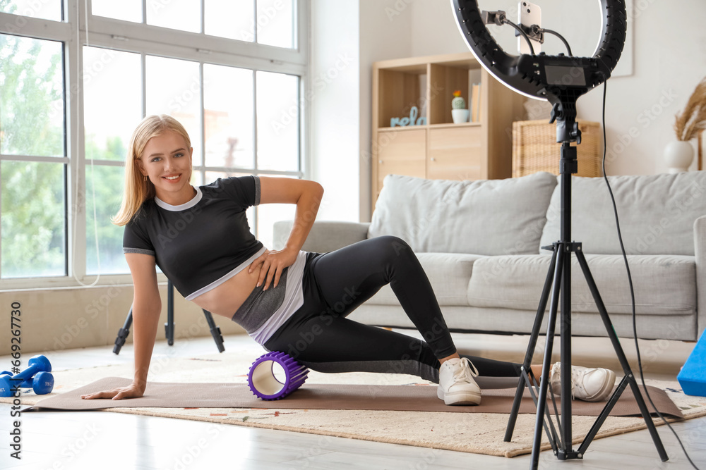 Beautiful young sport blogger recording video while training with roller at home