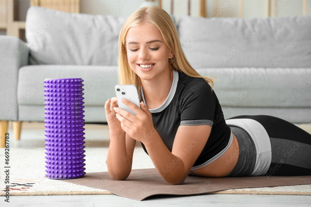 Beautiful young sport blogger recording video while training with roller at home