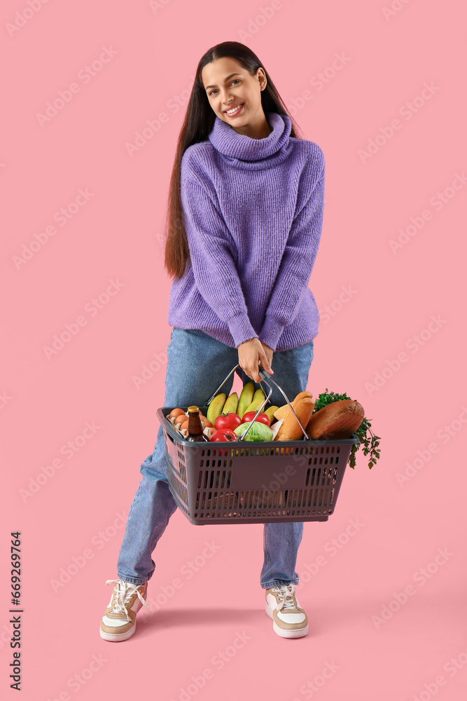 Young woman with shopping basket on pink background