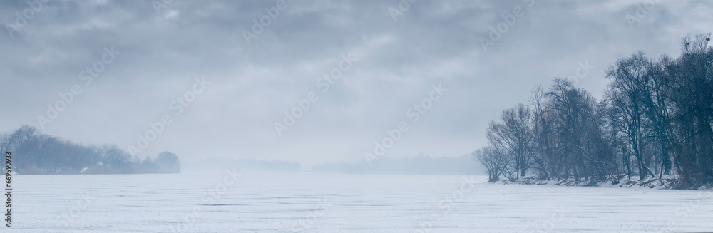 Winter landscape with river and trees on the river bank in cloudy weather