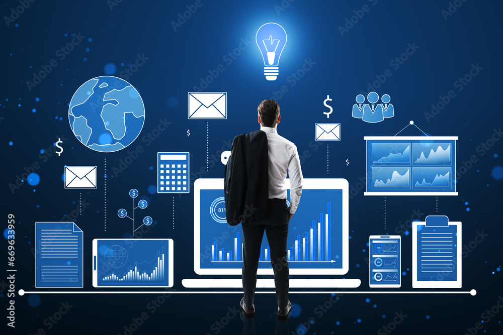 Back view of young european businessman looking at financial data and accounting hologram with devices and charts on blue background. Statistic research and technology concept.