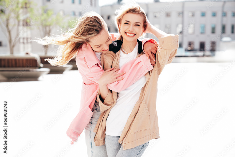 Two young beautiful smiling hipster female in trendy summer clothes. Carefree women posing in the street. Positive models having fun outdoors at sunny day. Cheerful and happy. Wind blows hair