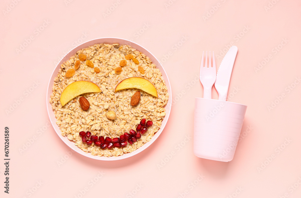 Plate of funny oatmeal for children and cutlery on pink background