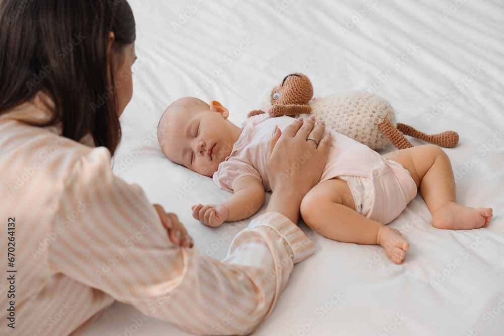 Mother and little cute baby with toy sleeping on bed at home