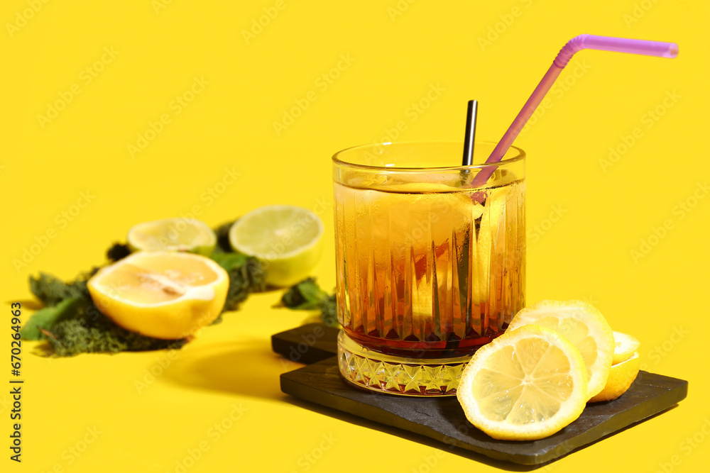 Cutting board with glass of Long Island iced tea and citrus fruits on yellow background