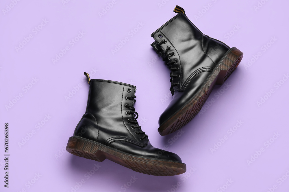 Stylish black leather boots on lilac background