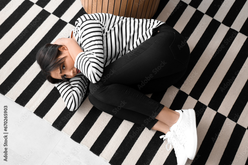 Beautiful young afraid woman lying on floor in living room