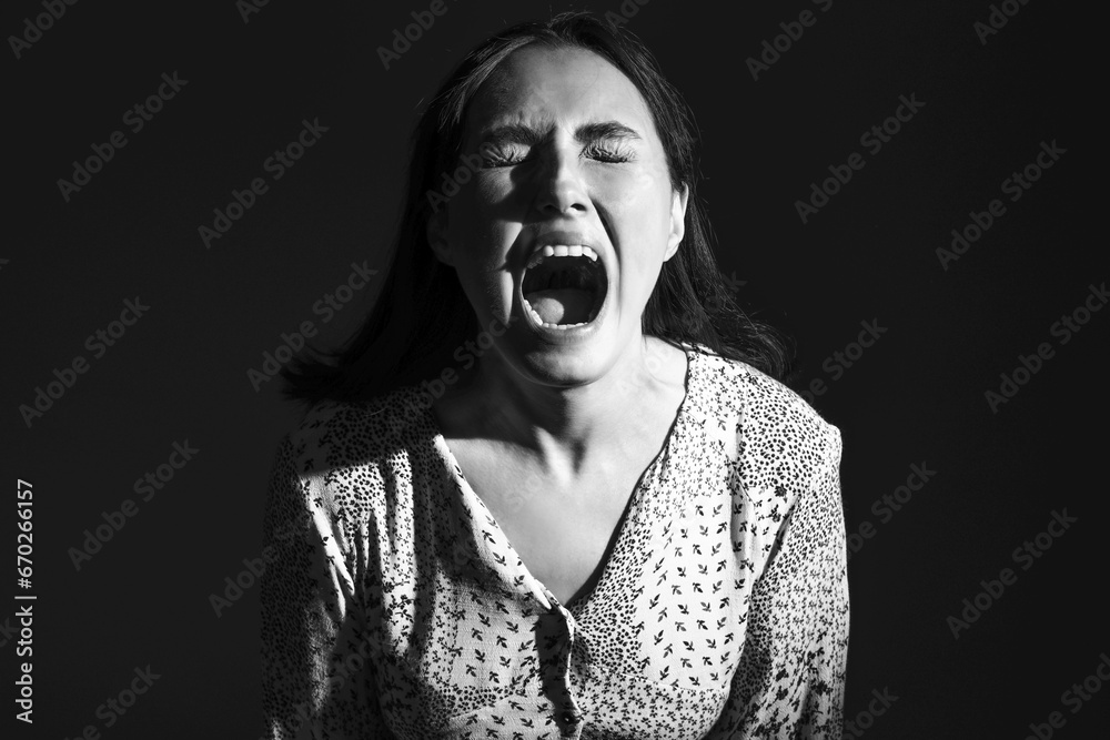 Beautiful young afraid woman screaming on black background