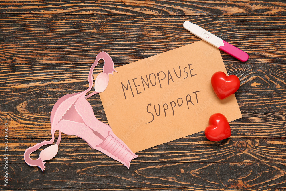 Paper with text MENOPAUSE SUPPORT, uterus, hearts and pregnancy test on wooden background