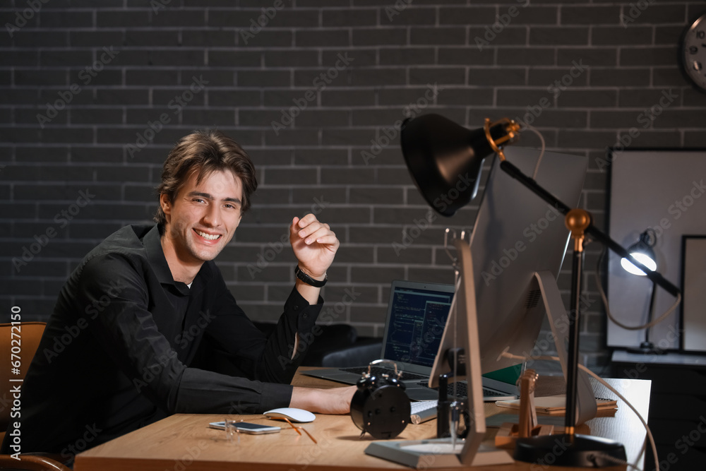 Happy young male programmer working with computers in office at night