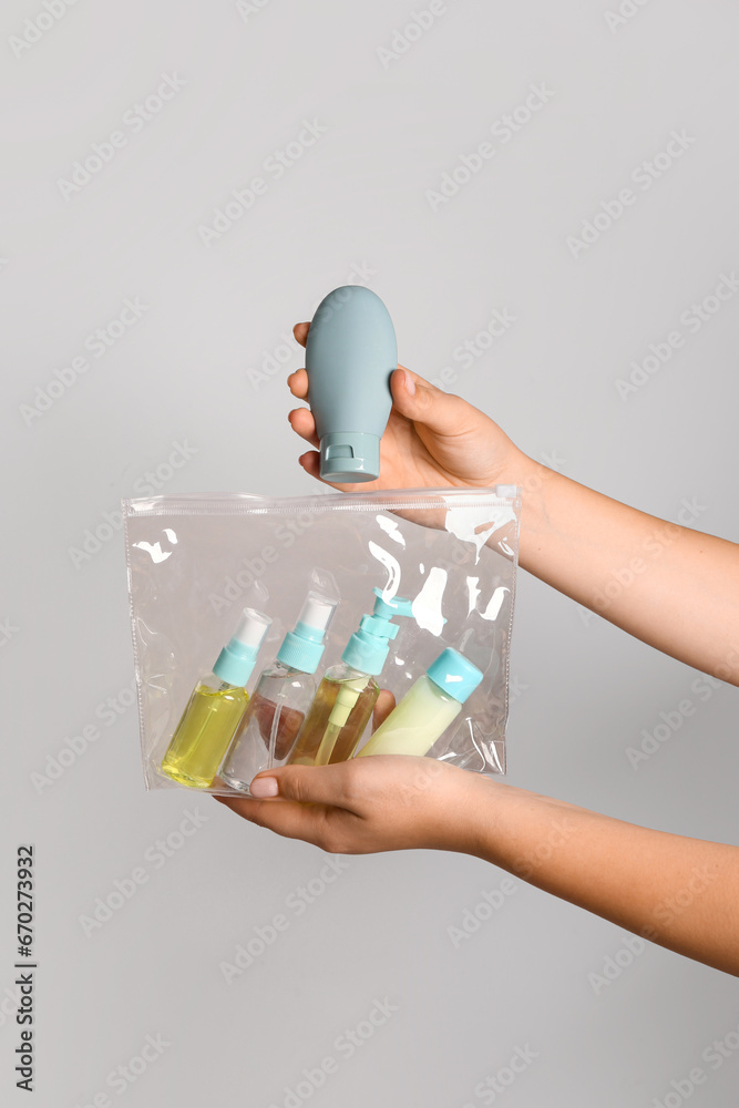 Female hands with bag of travel cosmetics on grey background