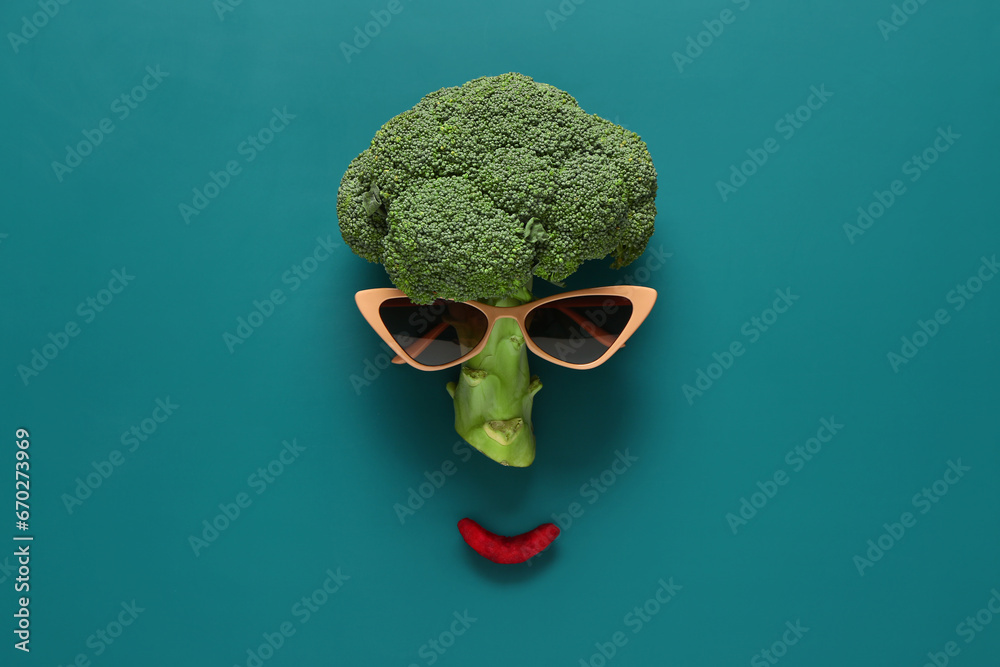 Funny face made of fresh broccoli and sunglasses on color background