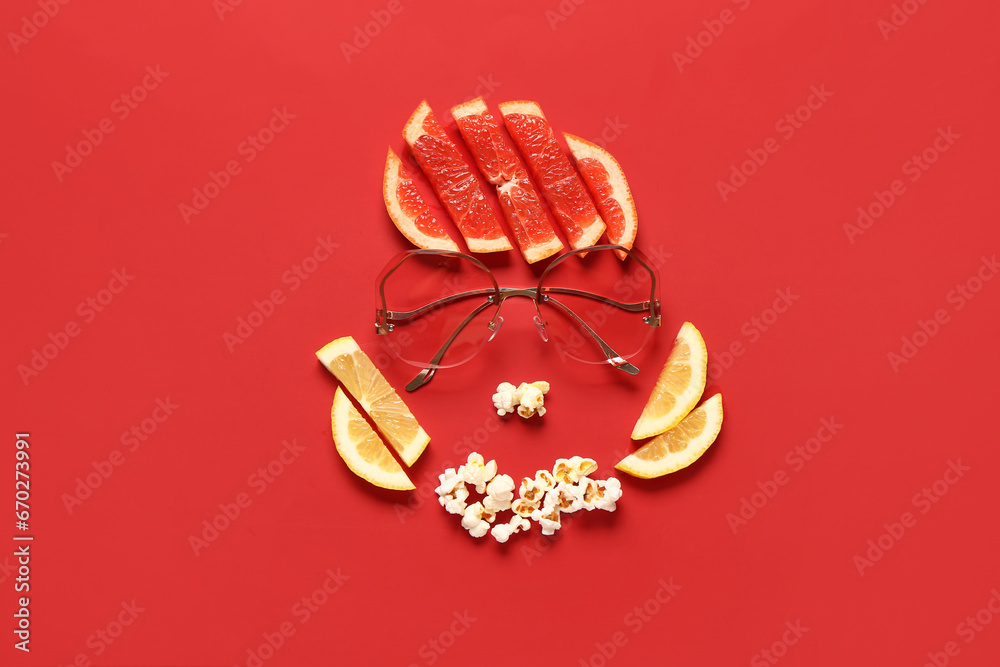 Funny face made of citrus fruits, popcorn and sunglasses on red background