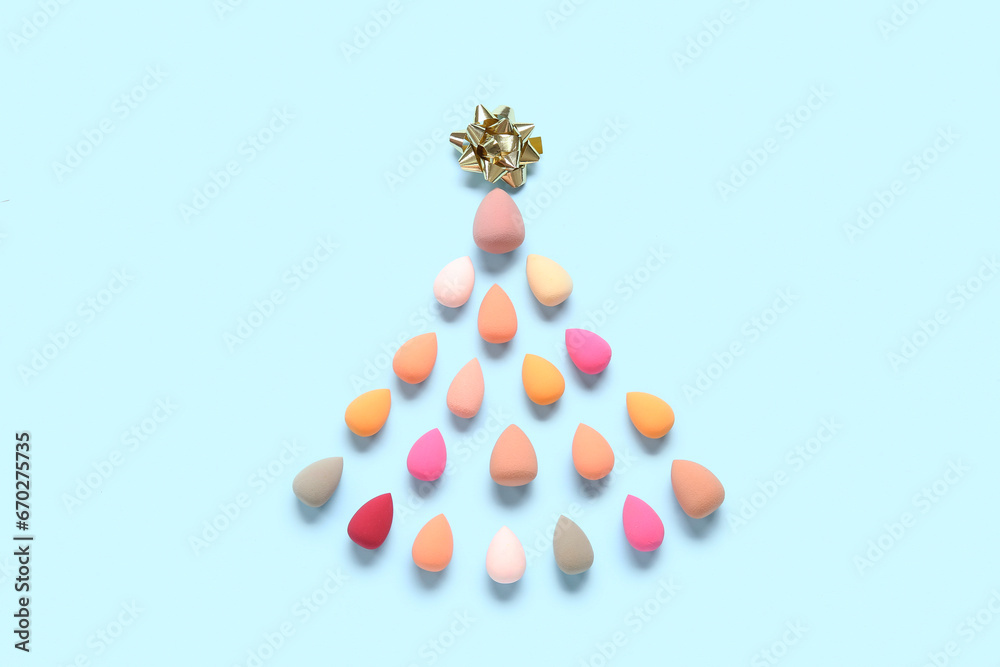 Christmas tree made of colorful makeup sponges and bow on blue background