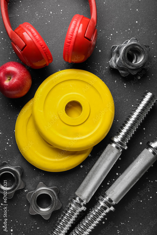 Barbell plates, grips, apple, headphones and clamps on black background