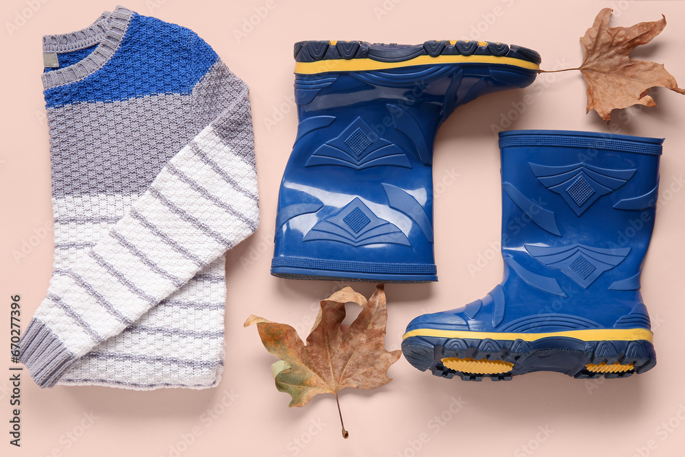 Blue gumboots with sweater and autumn leaves on color background