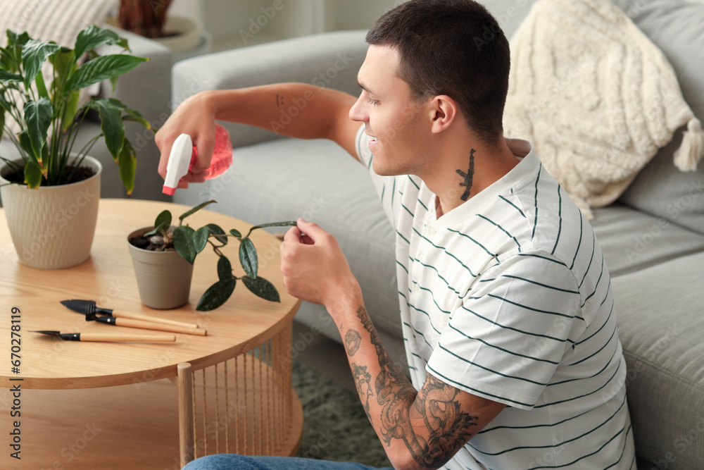 Young man watering plant at home