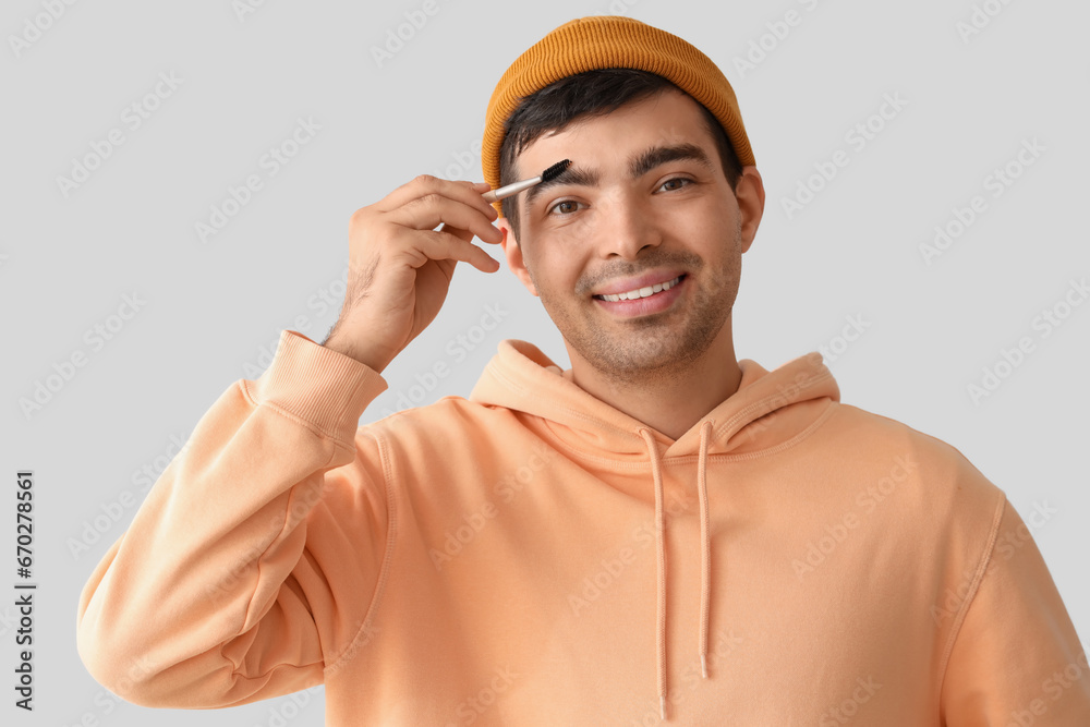 Male makeup artist with eyebrow brush on light background, closeup