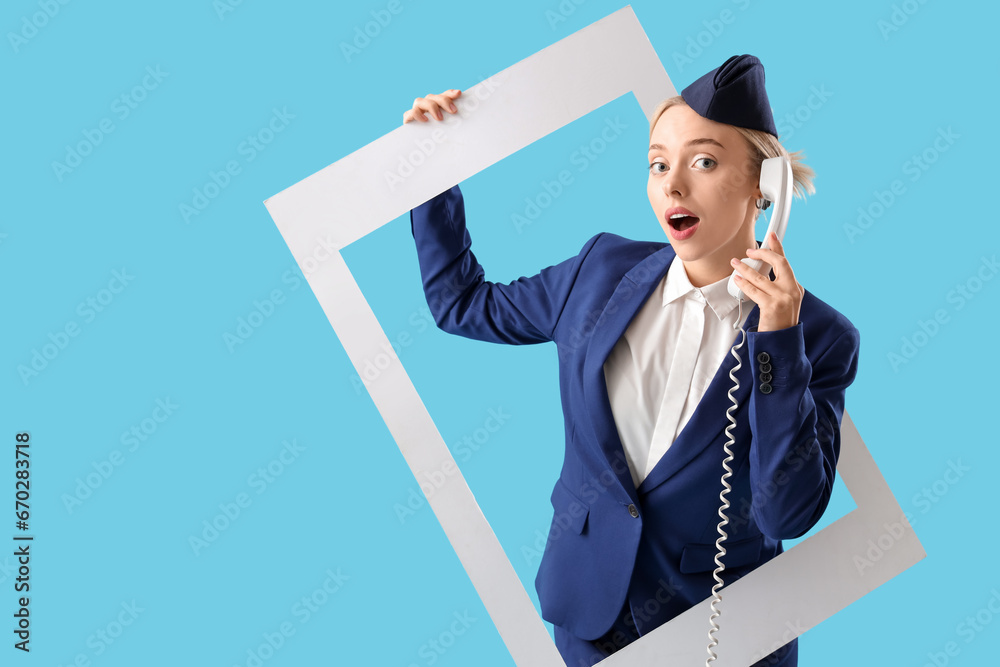 Shocked young stewardess with phone receiver and frame on blue background