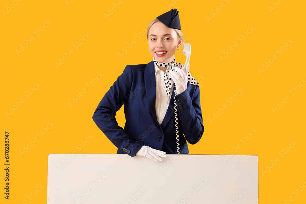 Young stewardess with phone receiver and blank poster on yellow background