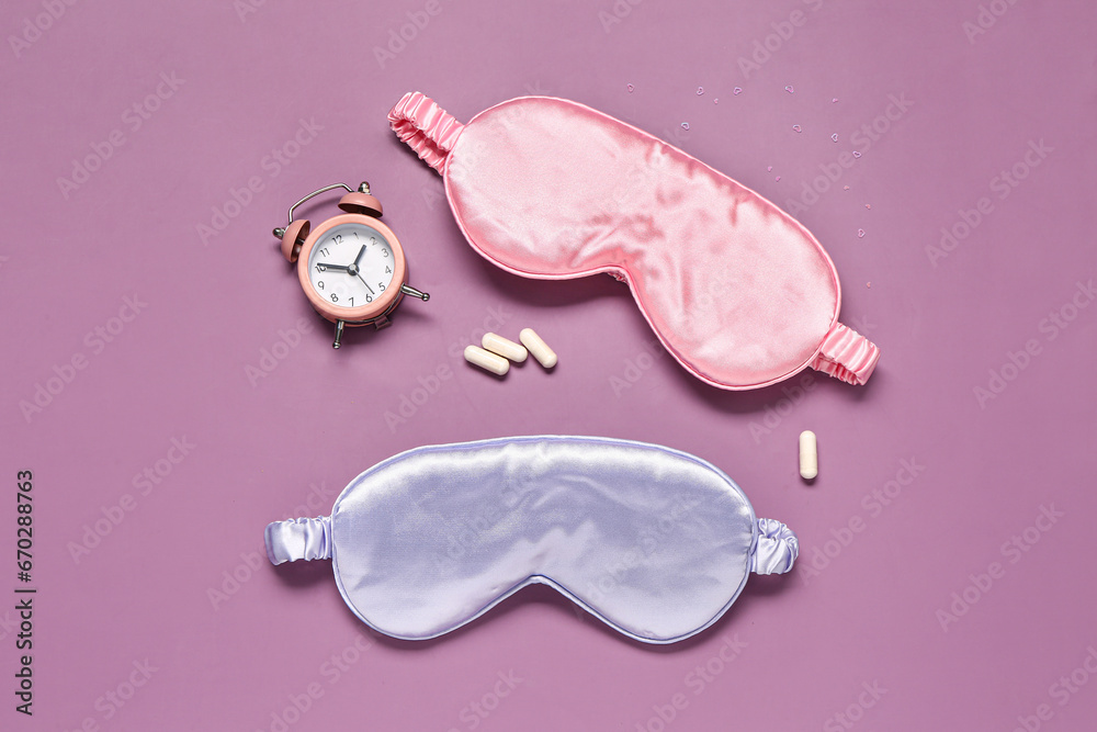 Stylish sleep masks, pills and alarm clock on color background