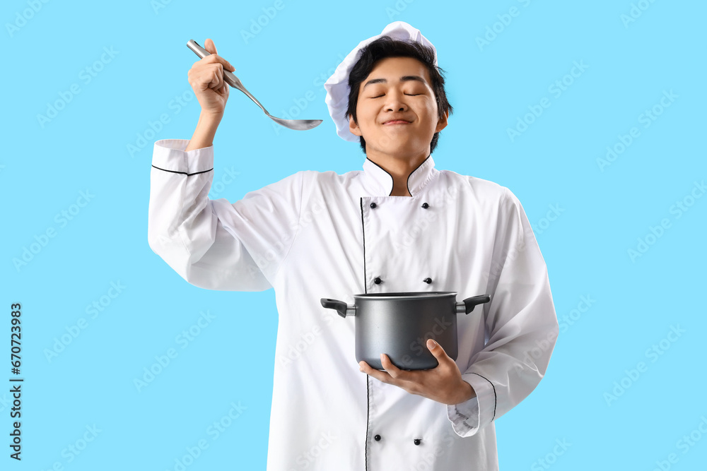 Male Asian chef with ladle and cooking pot on blue background