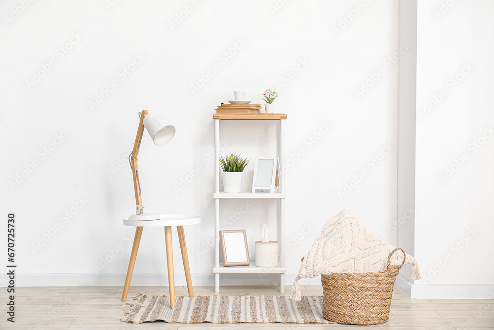 Desk lamp on small table and shelving unit with decor near white wall