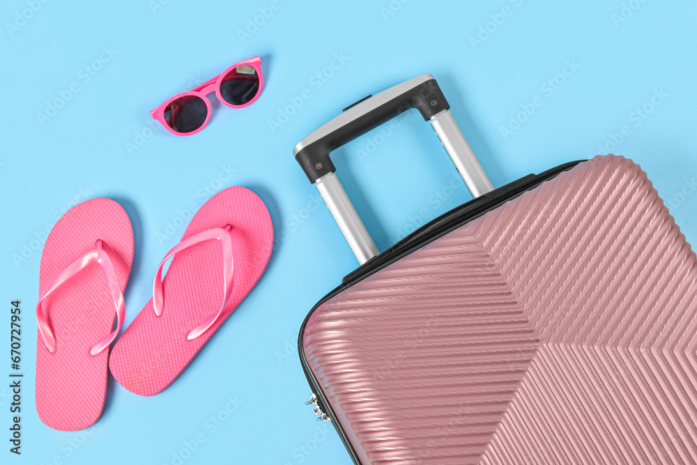 Stylish suitcase, flip-flops and sunglasses on color background