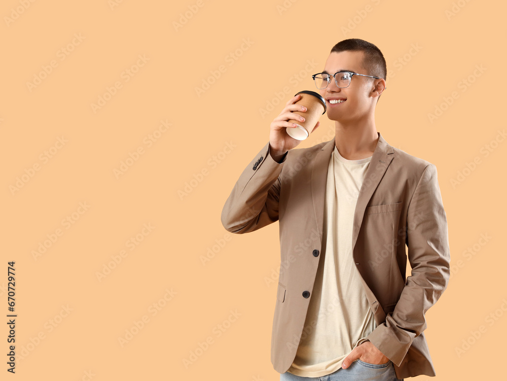 Handsome young businessman with cup of coffee on orange background