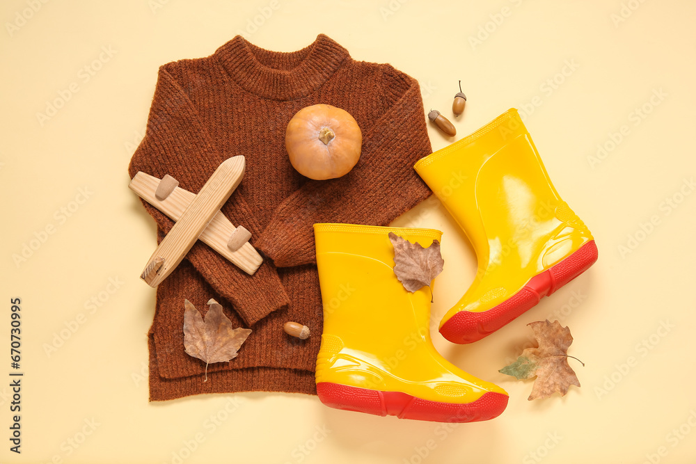 Yellow gumboots with sweater, pumpkin and autumn leaves on color background