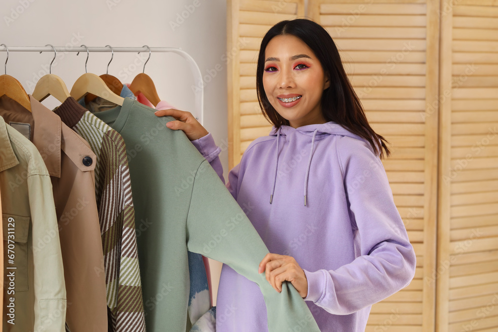 Young Asian woman near clothes rack at home