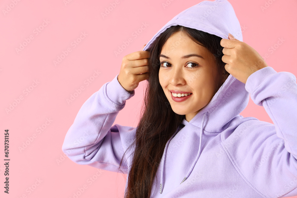 Beautiful young Asian woman in stylish hoodie on pink background