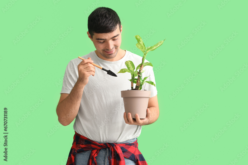 Young man with shovel and plant on green background