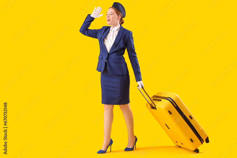 Young stewardess with suitcase on yellow background