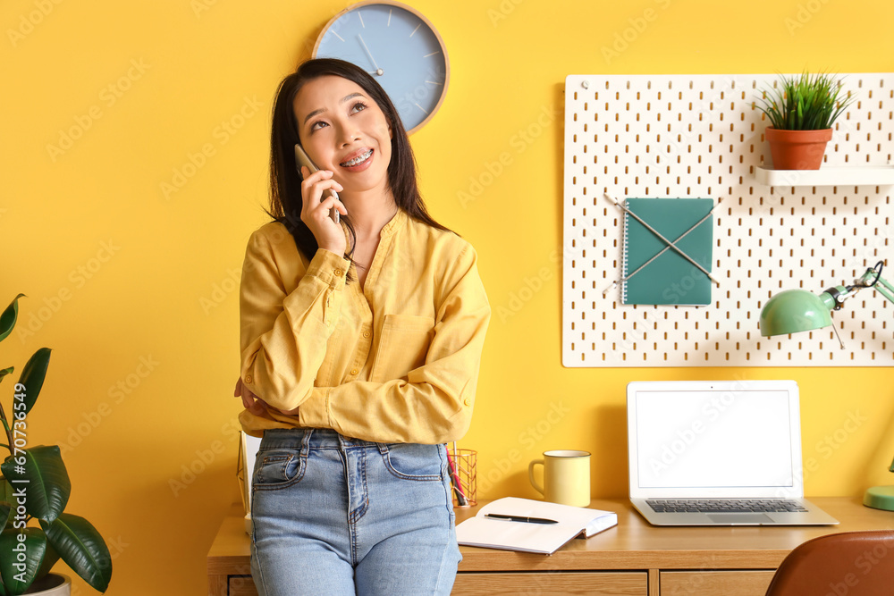 Young Asian woman talking by mobile phone at home office