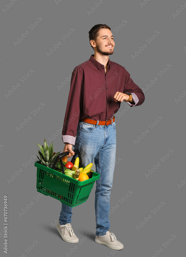 Young man with shopping basket on grey background