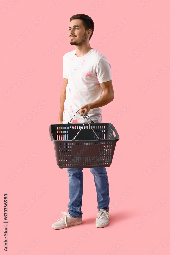 Young man with shopping basket on pink background