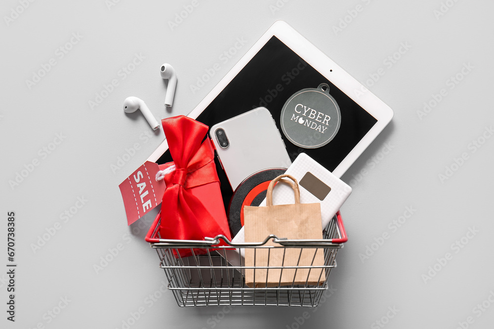 Shopping basket with different gadgets and gift box on grey background. Cyber Monday sale