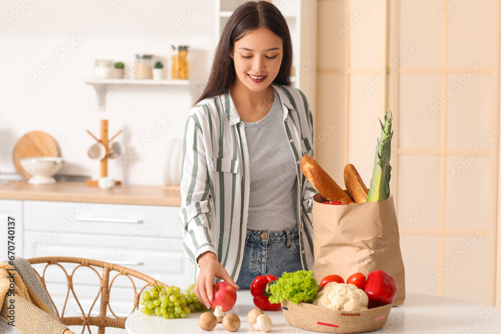 Young Asian woman unpacking fresh products from market at table in kitchen