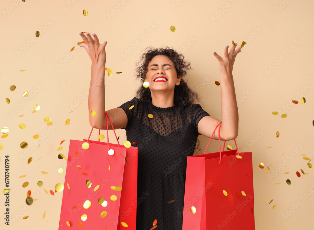 Beautiful African-American woman with shopping bags and confetti on beige background. Black Friday sale