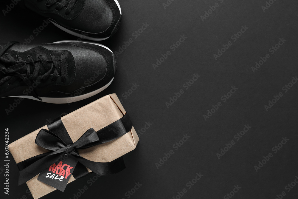 Stylish male sneakers and gift box on dark background. Black Friday sale