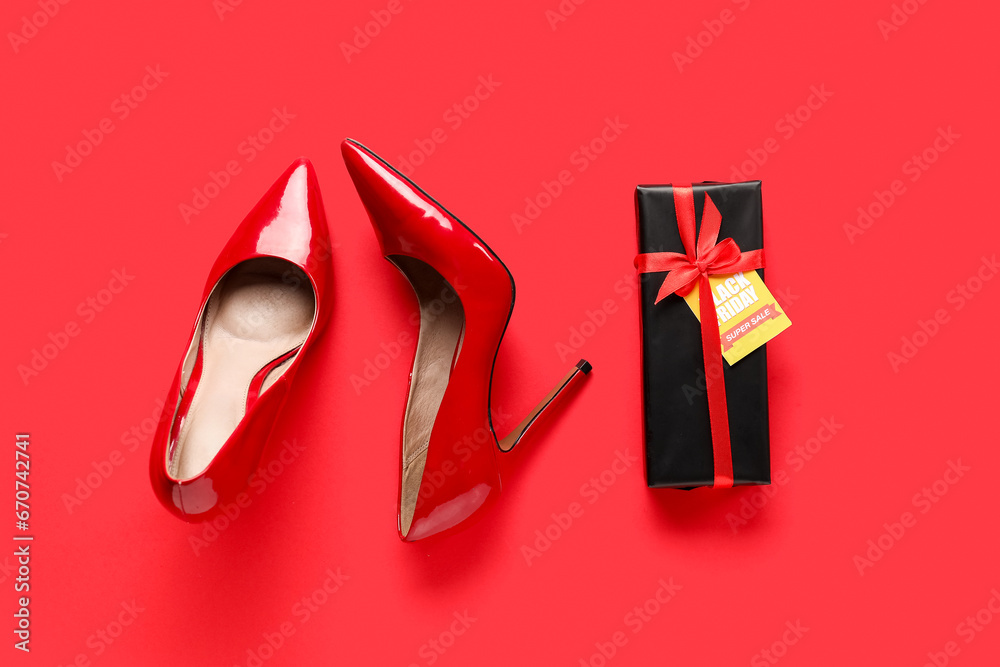 Stylish high heeled shoes and gift box with sale tag on red background. Black Friday