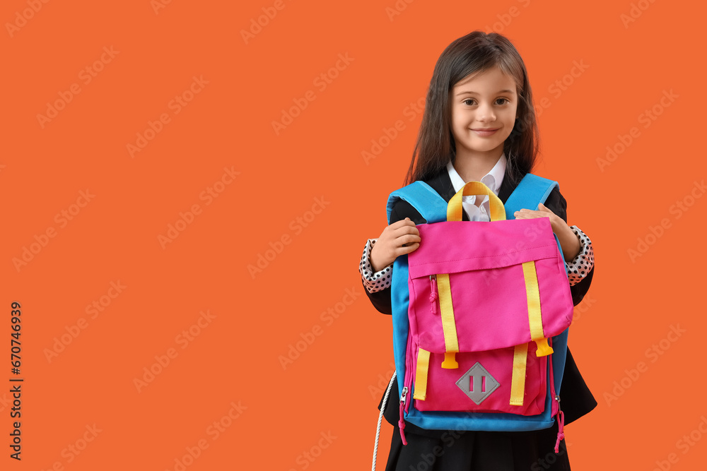 Cute little schoolgirl with backpack on orange background