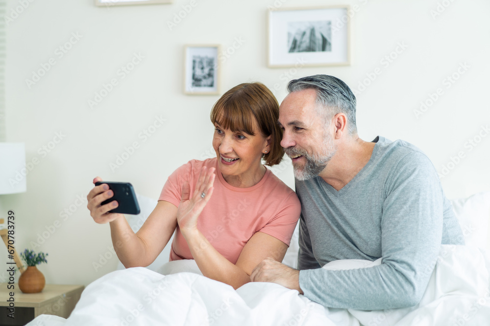 Caucasian senior couple video call with family in bedroom in house. 