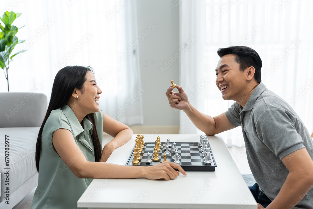 Asian attractive couple playing chess game in living room at home.